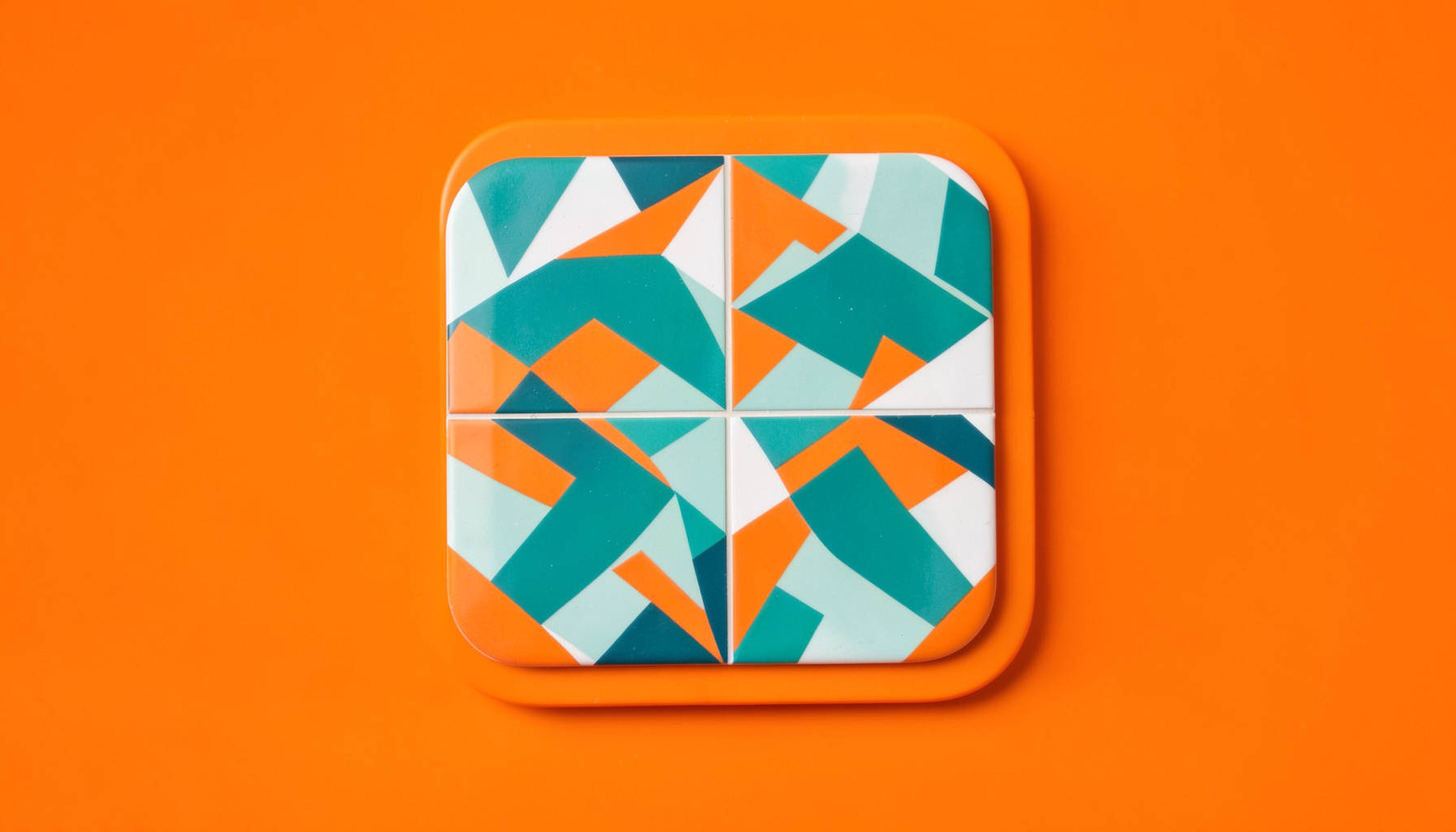 A clean studio photograph on a seamless light backdrop of a rounded tile featuring a teal and orange interlocking geometric design, softly shadowed.